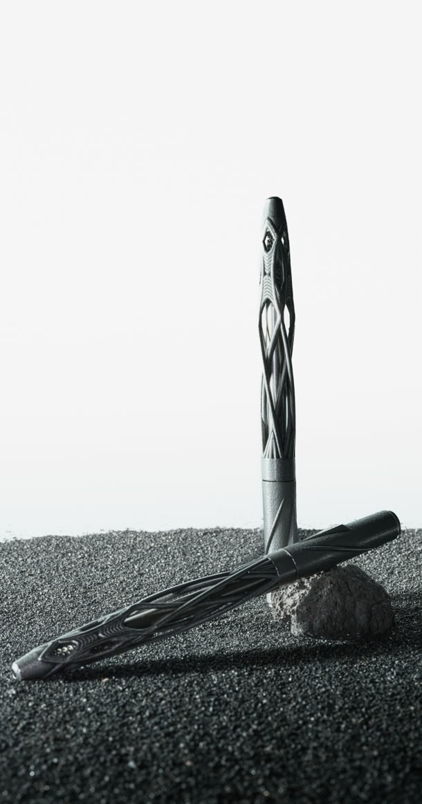 Virga pen by Varydes standing in black sand, showing open stainless steel lattice structure